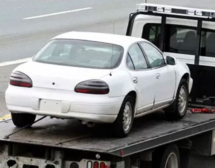 Flatbed truck towing a white car, representing the Cash for Old Cars program in Brisbane.